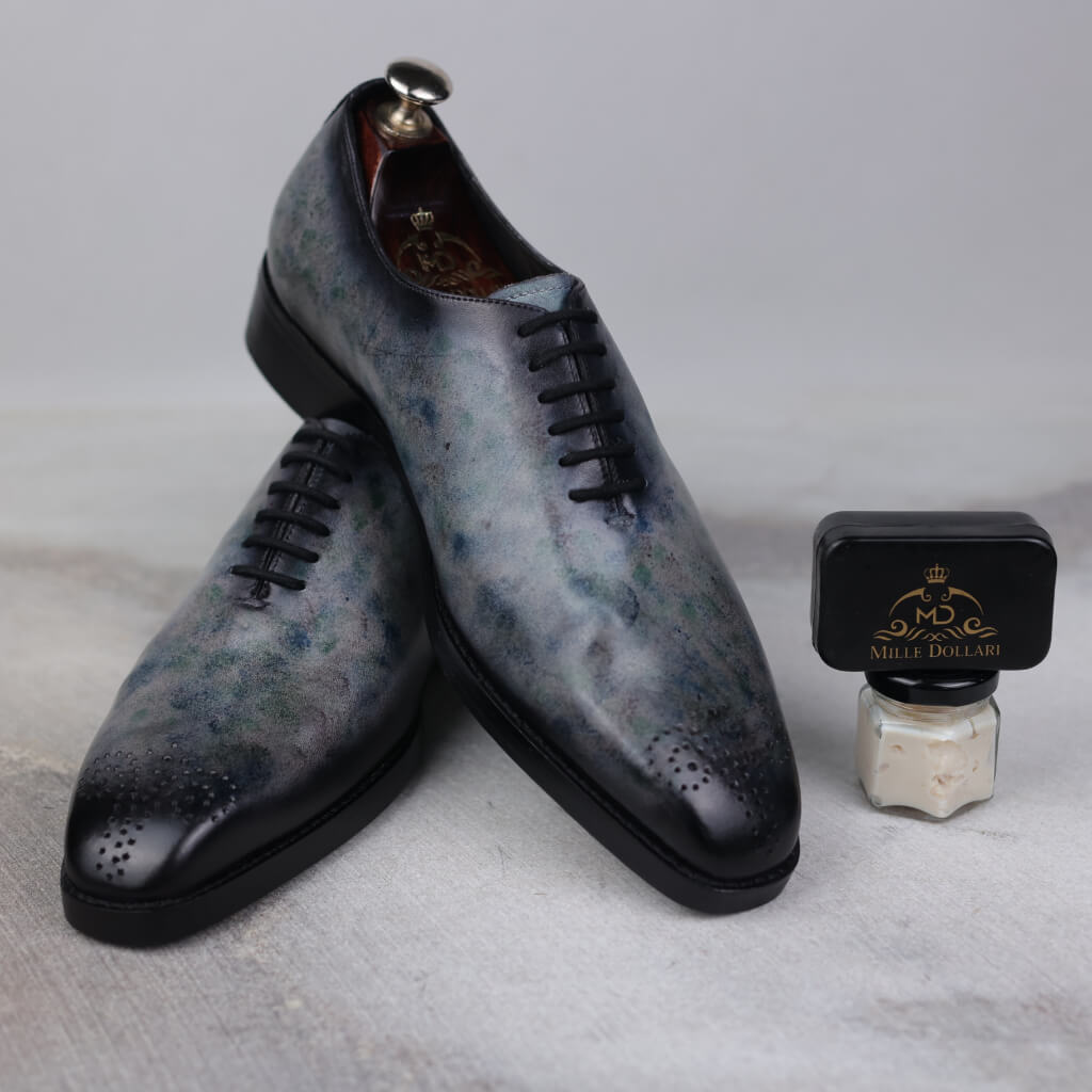 A pair of Eclipse Elegance Wholecut Derby Shoes crafted from Argentina white crust leather with a sophisticated grey marble patina. Featuring a durable Italian leather sole with a leather welt, leather insole, and memory foam cushioning for ultimate comfort, these shoes offer a premium, refined look for any occasion and come with a 6-month warranty.