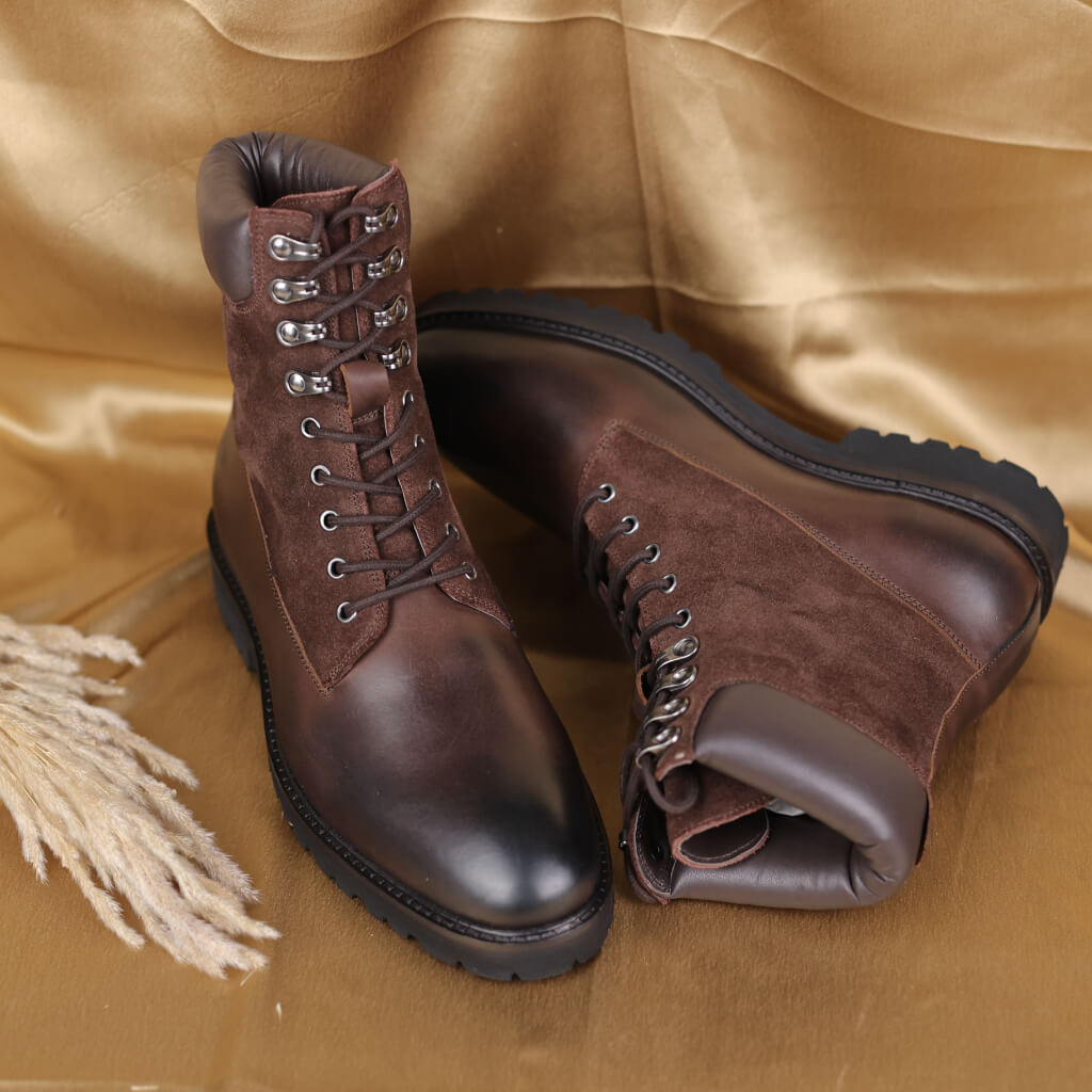 A pair of high-angle hiking luxury combat boots crafted from premium brown burnished and suede leather. The combination of materials offers a rugged yet refined look, ensuring durability and a unique textured finish for both style and functionality.