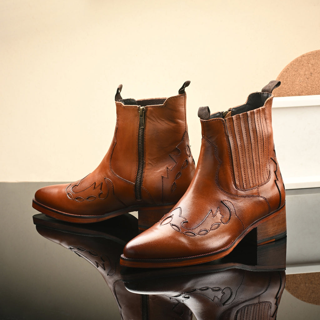 "Western-style cowboy boots in premium brown leather with intricate laser-cut detailing, elastic side panels, and sturdy wooden heels—perfect for rugged elegance and versatile styling."