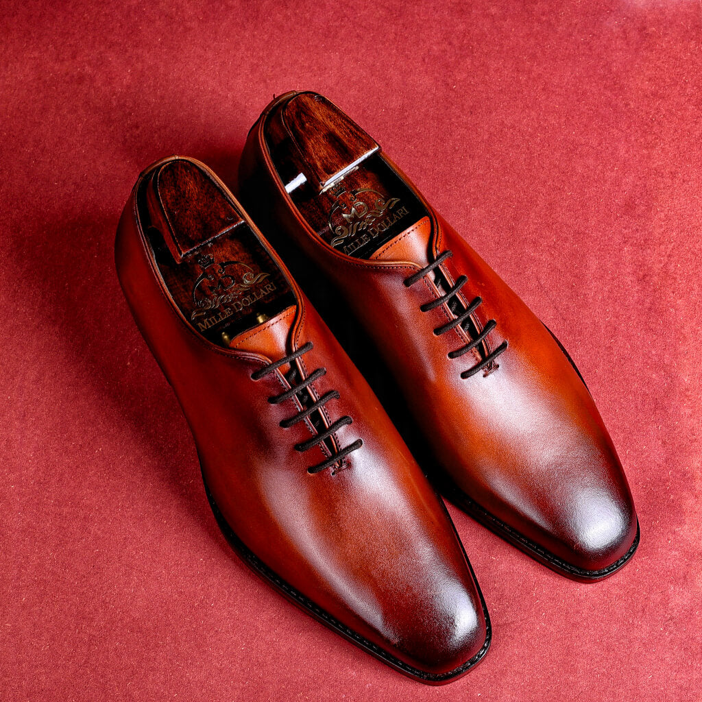 A close-up of the Mille Regalia wholecut derby shoe by Mille Dollari, crafted from Argentina crust leather. The shoe features a hand-painted deep brown finish, Italian leather sole with TPR grip for anti-skid properties, and an insole with memory foam cushioning for comfort. The luxurious design emphasizes elegance and craftsmanship, making it suitable for both business meetings and formal events.