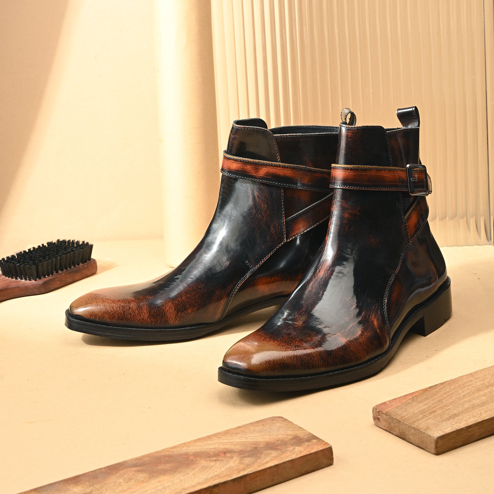 Pair of Mille Dollari Verona men's ankle boots in burnished brown and black leather with a high-shine patina finish and a silver side buckle strap, photographed on a white background.