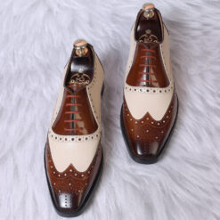 A pair of Brown and White Mirror Glossed Spectator Wingtip Oxfords displayed on a wooden surface, highlighting the intricate wingtip detailing and glossy finish.