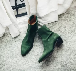 A pair of dark green suede leather Fiorina slip-on boots for men, featuring a sleek pointed-toe design and a convenient side zipper. These boots, part of the AW24 collection, exude sophistication with their rich suede texture and premium craftsmanship, ideal for elevating formal or casual looks.